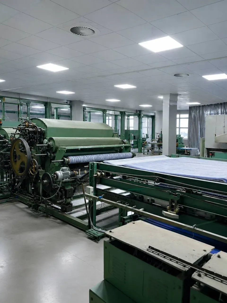 Close-up of the delivery section of a drawing frame processing and drafting a blend of green and white textile fibers.